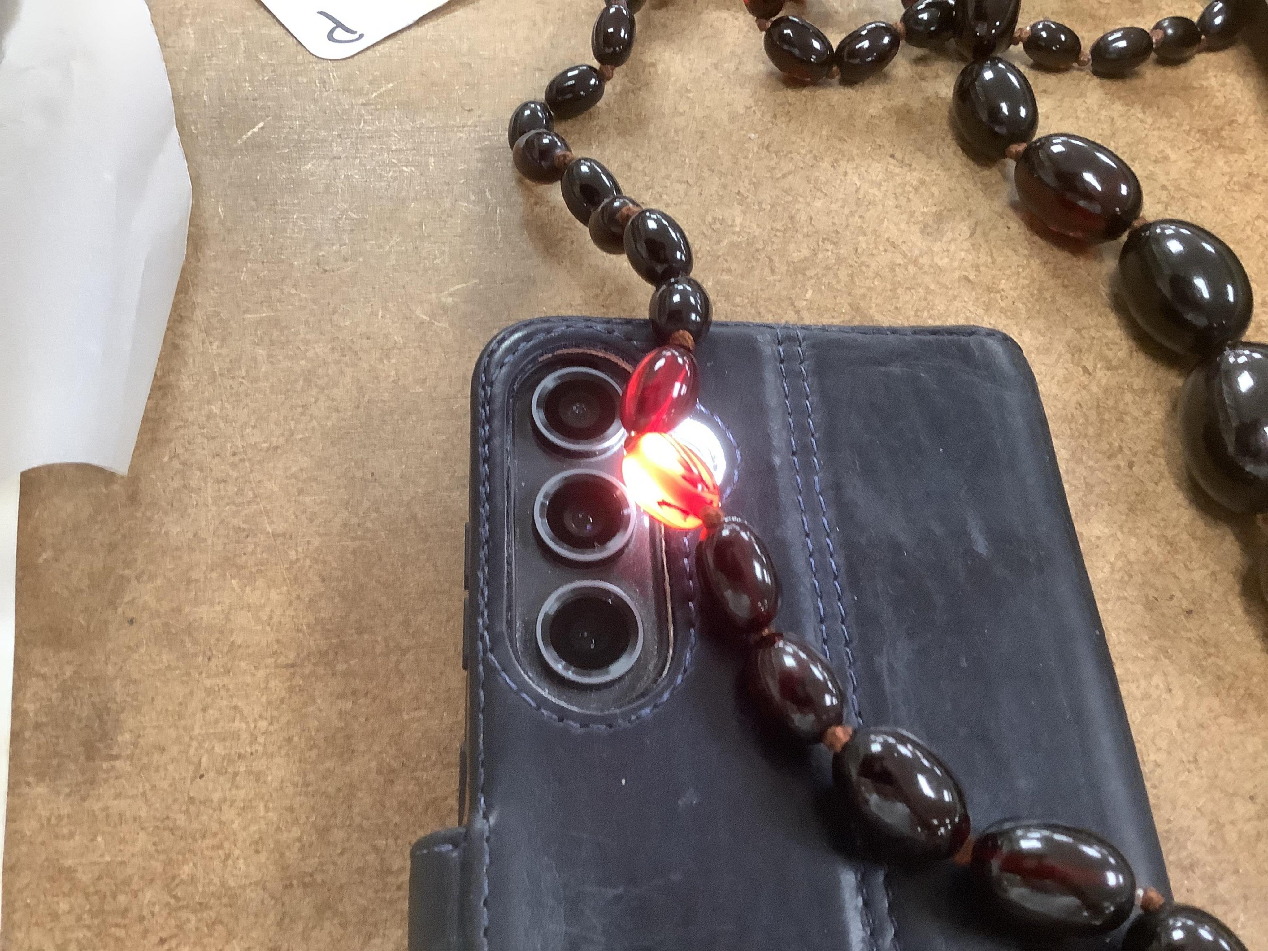 A single strand graduated simulated oval dark cherry amber bead necklace, 110cm, gross weight 90 grams.
